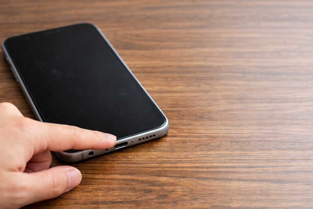 スマホの下部にあるマイク穴を指で示している様子の写真