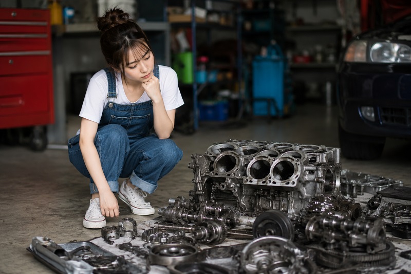 オーバーホール中のエンジンを見ているオーバーオールを着た女性の画像